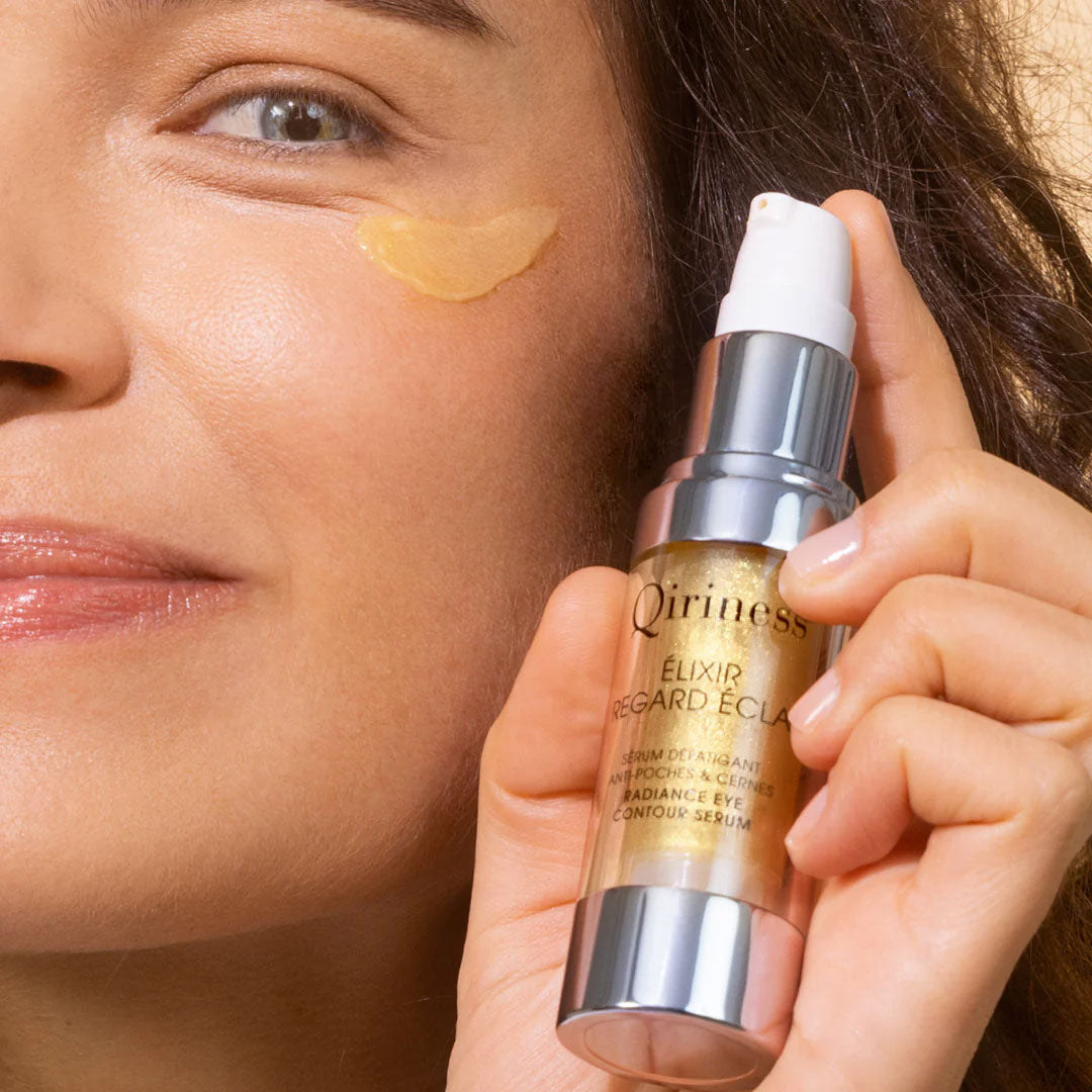 Sérum Qiriness en flacon transparent avec bouchon doré posé sur une surface blanche, soin anti-âge hydratant.